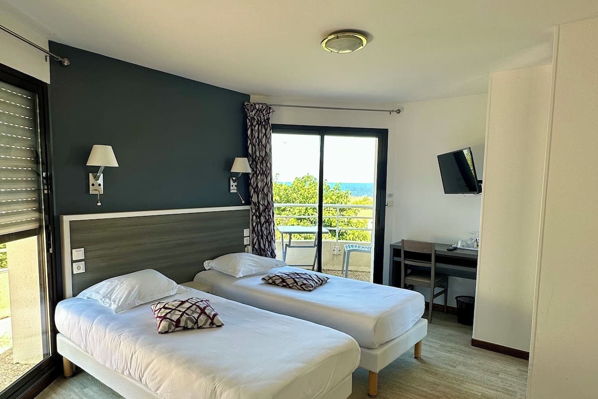 A hotel room with two beds, a desk, a TV, and a balcony with a view.