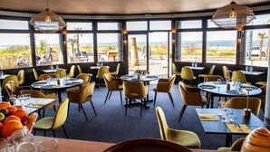 A restaurant with round tables and yellow chairs, large windows with a view of the beach, and hanging light fixtures. - Hotel Castel Moor (Le Croisic)