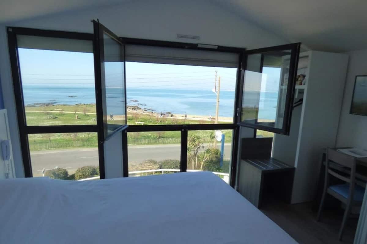 A bedroom with a large bed, a desk, and a view of the sea.