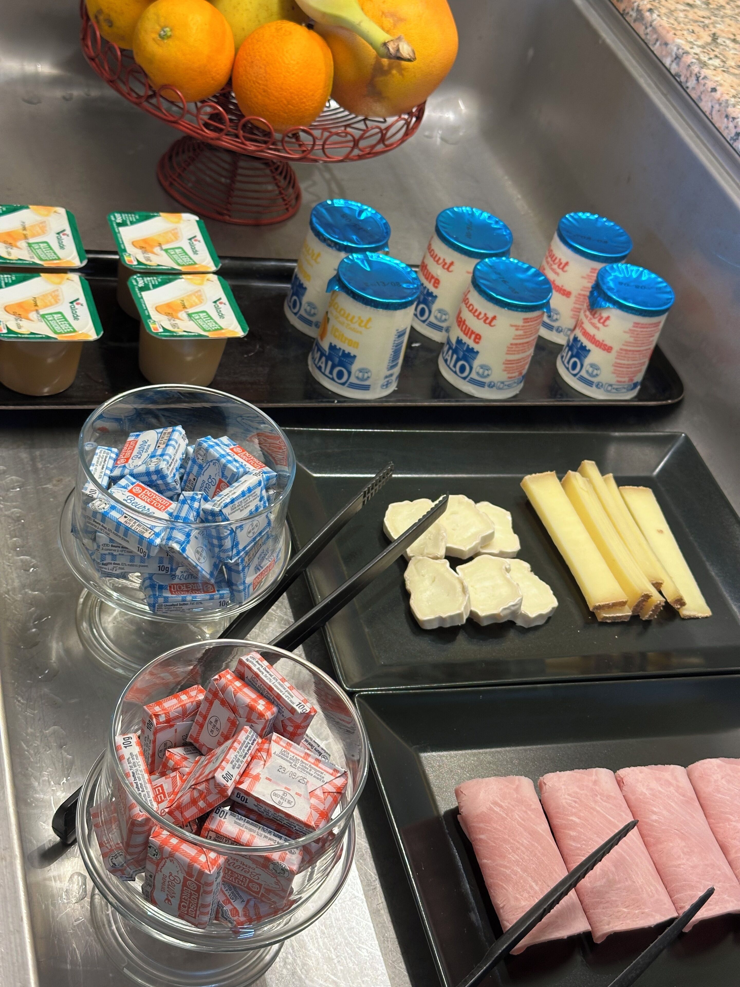 Un comptoir de cuisine sur lequel on trouve divers aliments, notamment un panier d’oranges, des pots de yaourt, des collations emballées et des tranches de viande.
