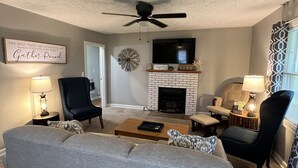 A living room with a gray sofa, a wooden coffee table, a fireplace, and a ceiling fan. - The Gatehouse, 2-bedroom house in charming Gamaliel with WiFi, AC, pet friendly. (Gamaliel)