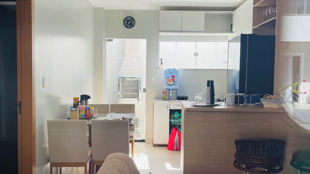 A modern living room with a sofa, a coffee table, and a TV. There is a kitchen area with cabinets and a refrigerator. - Cozy house facing east, in a gated community - Salinópolis/PA (Salinópolis)