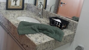 A bathroom with a granite countertop, a sink, a mirror, and a door. - Cozy house facing east, in a gated community - Salinópolis/PA (Salinópolis)