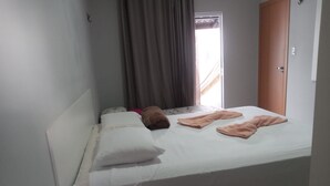 A small, simple hotel room with a single bed, a bedside table with a remote control, and a door to the right. - Cozy house facing east, in a gated community - Salinópolis/PA (Salinópolis)