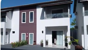 A two-story residential building with a flat roof, white and maroon exterior walls, and a balcony on the upper floor. - Cozy house facing east, in a gated community - Salinópolis/PA (Salinópolis)