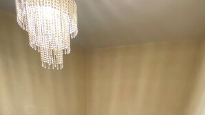 Ein Zimmer mit weißer Decke, einem Chandelier, einem Gemälde an der Wand und einem teilweise gefliesten Boden.