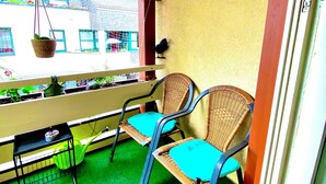 Ein Balkon mit zwei Korbstühlen, einem kleinen Tisch und einer hängenden Pflanze.