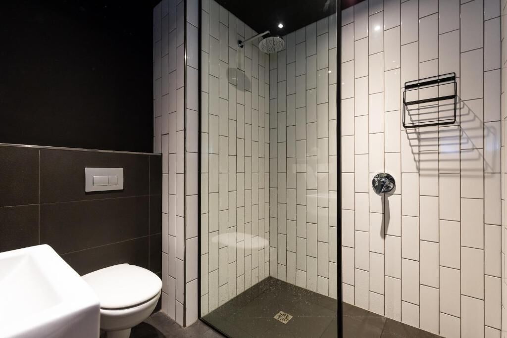 A modern bathroom with a glass-enclosed shower, white tiled walls, a white toilet, and a black sink.