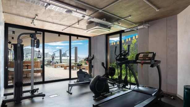 A modern gym with cardio equipment, weight machines, and a large window offering a city view.