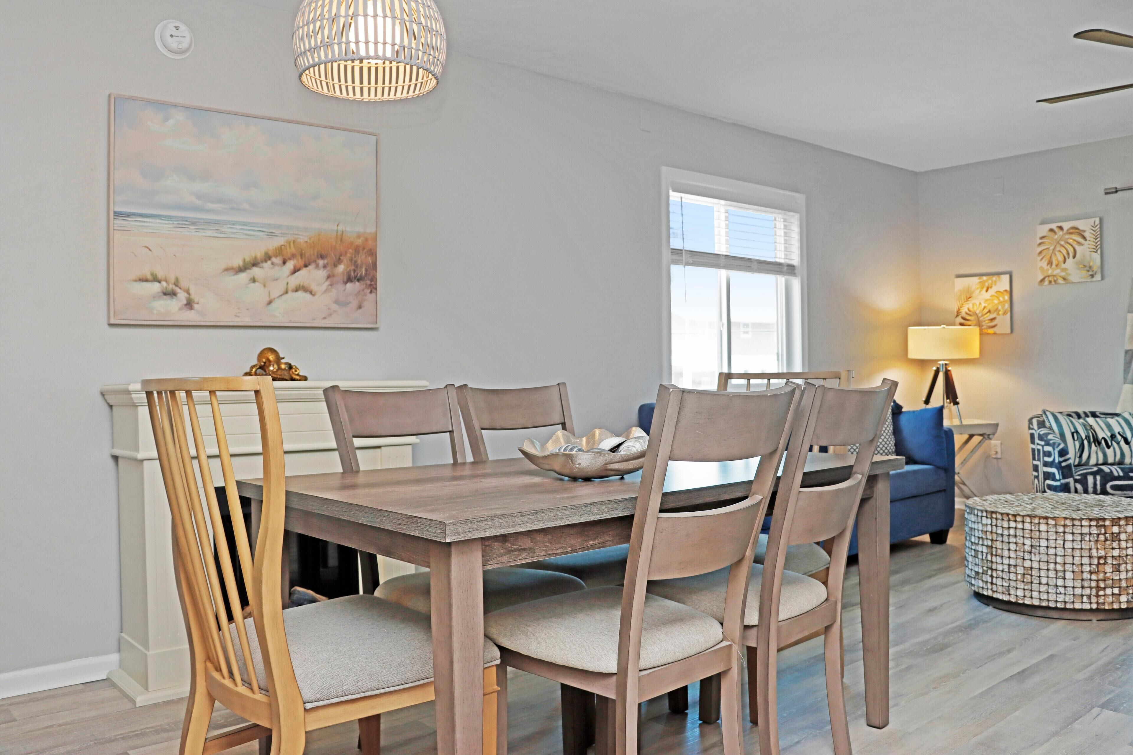A dining area with a wooden table and chairs, a fireplace, and a painting of a beach scene.