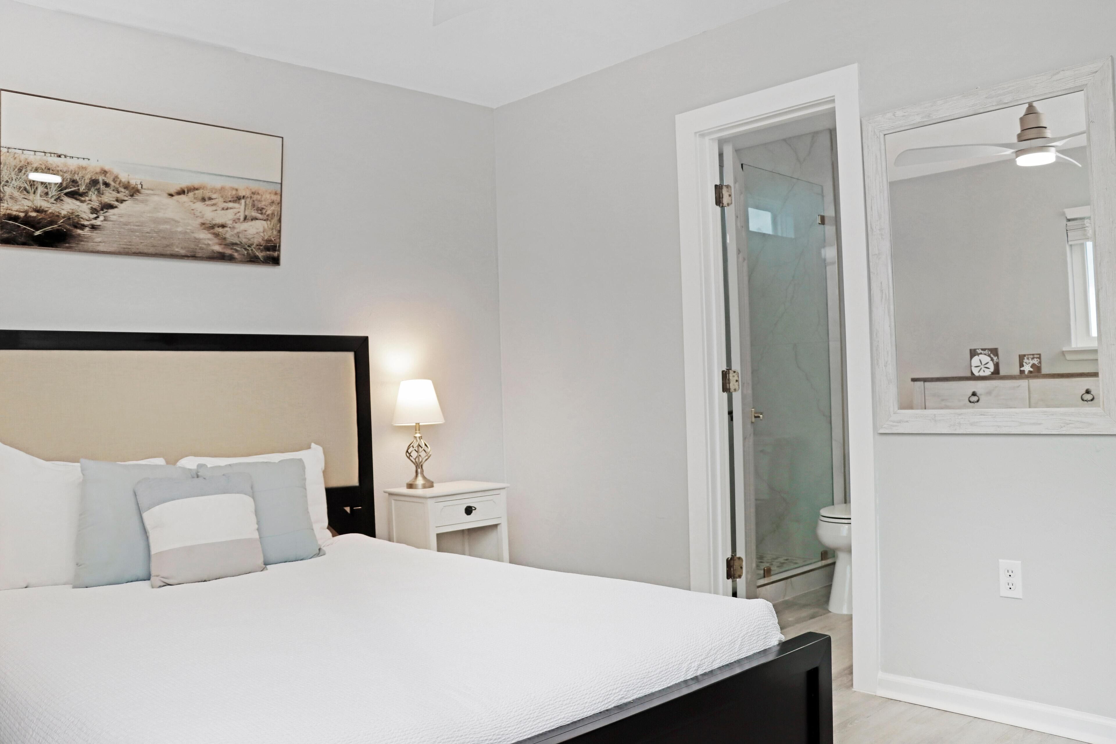 Een slaapkamer met een bed, nachtkastje, lamp en een lijst met een afbeelding aan de muur.