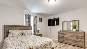 Una camera da letto con una testiera in legno, una coperta con motivi floreali, una televisione a schermo piatto, un comò e uno specchio.