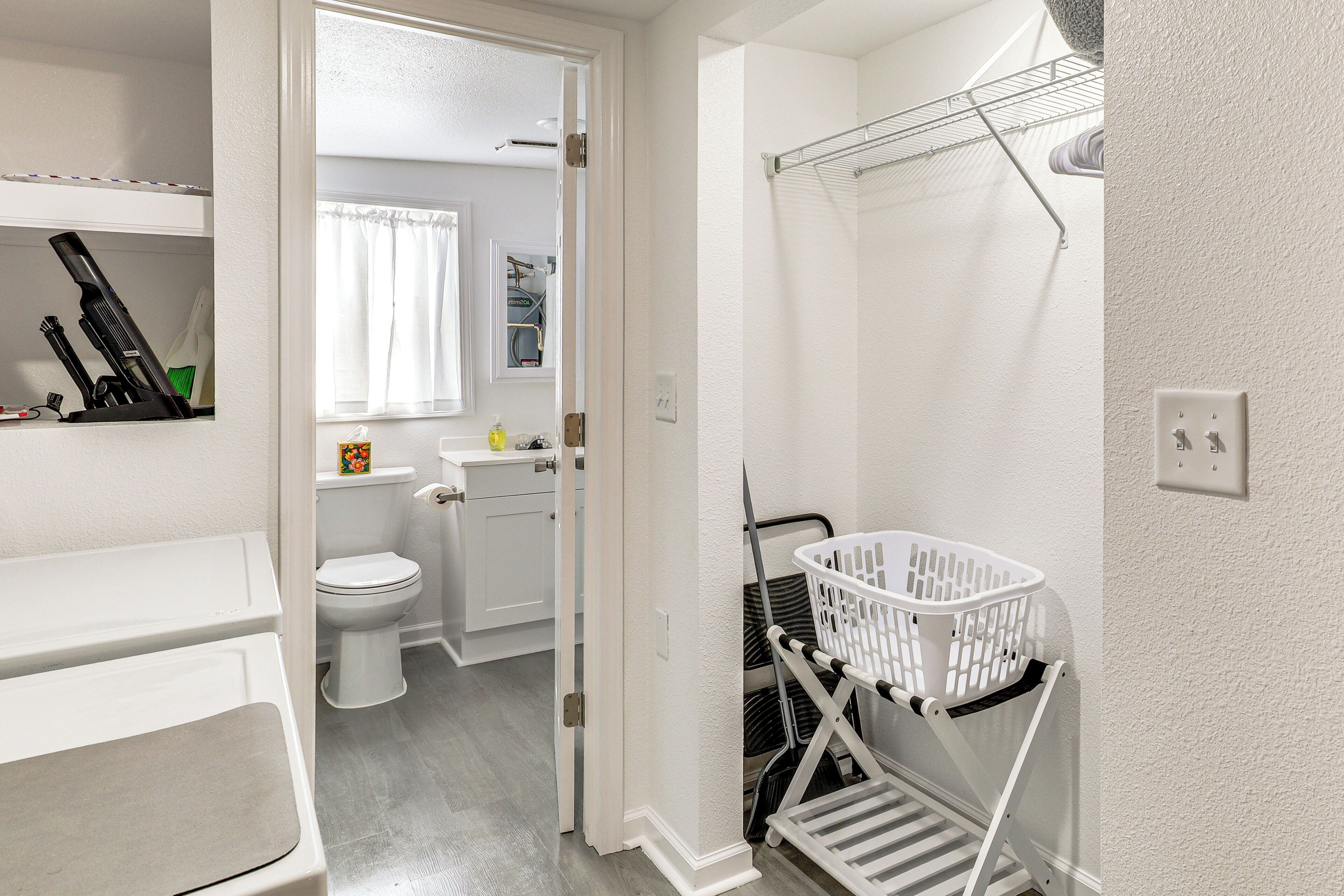 Un baño con inodoro, lavamanos y una cesta de ropa en un estante.