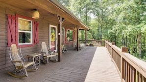 Een houten terras met schommelstoelen en een overdekte veranda met uitzicht op een bos.