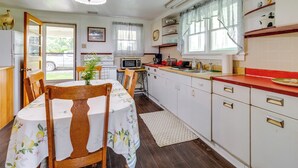 A kitchen with white cabinets, a wooden dining table with a floral tablecloth, a microwave, and a sink.