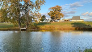 A calm lake with a dock, surrounded by trees and a building in the background.