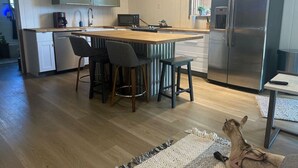 A modern kitchen with a central island, bar stools, a refrigerator, and a microwave.
