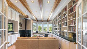 Un amplio salón con un sofá seccional color beige, una chimenea y una gran estantería llena de libros.