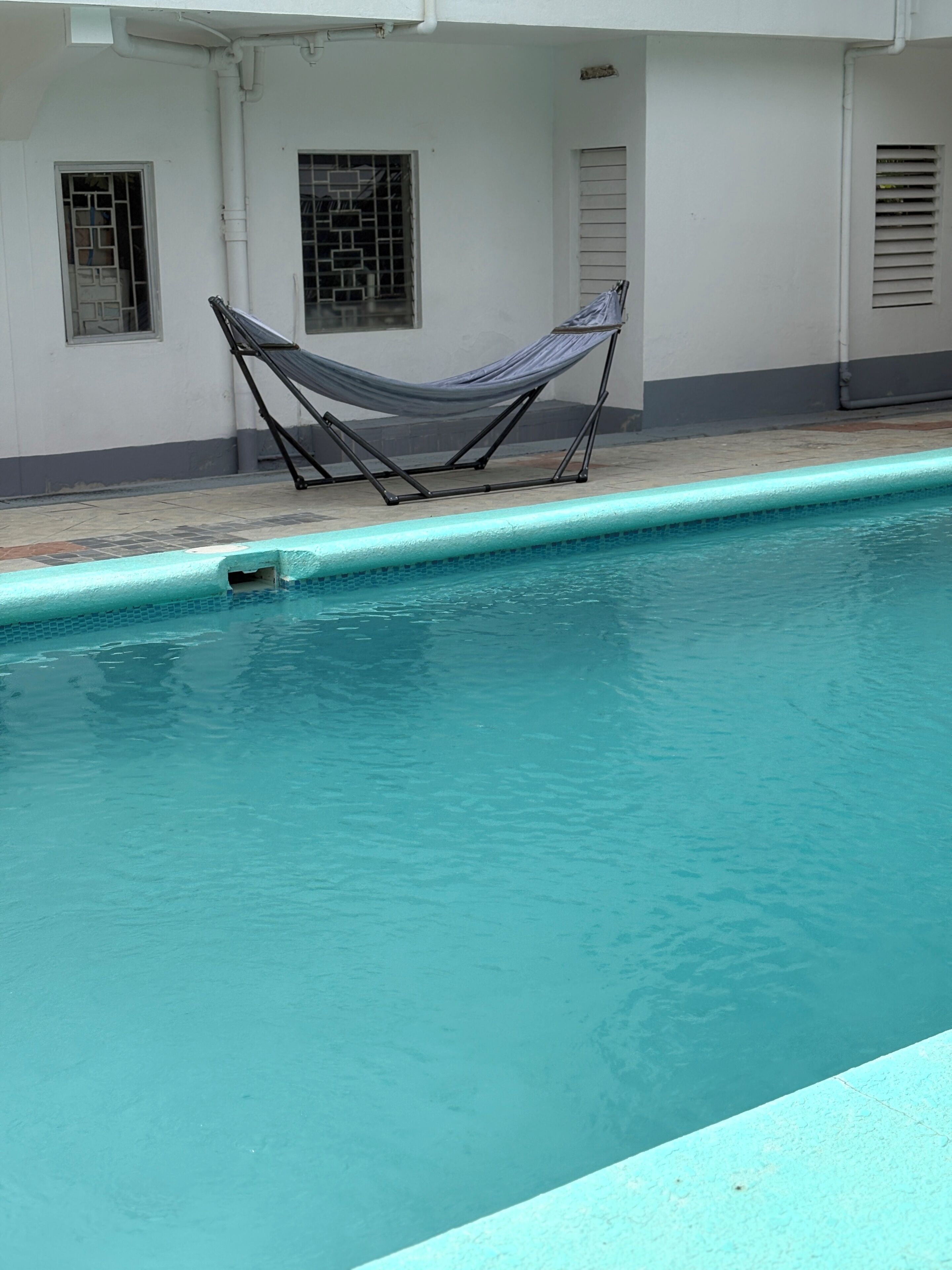 Una piscina con una silla hamaca y un borde con baldosas.