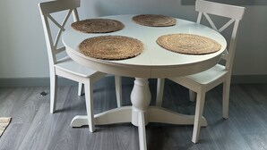 A dining table with four woven placemats, surrounded by white chairs, set against a light-colored wall with two framed wall art pieces above. - Charming 1-bedroom townhome in brilliant Hermosa Beach (Hermosa Beach)