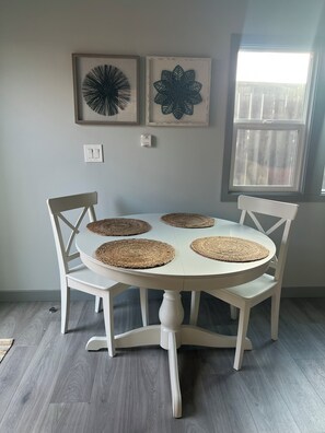 A dining table with four woven placemats, surrounded by white chairs, set against a light-colored wall with two framed wall art pieces above. - Charming 1-bedroom townhome in brilliant Hermosa Beach (Hermosa Beach)