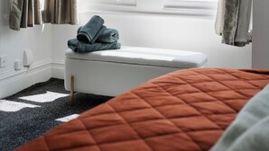 Una camera da letto con una finestra, un letto, una panca e vista sugli edifici.