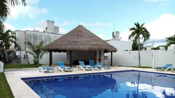 A swimming pool with lounge chairs and a thatched-roof structure. - Residencia Mejía · Descanso y Comodidad a Minutos del Mar Caribe (Playa del Carmen)