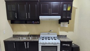 A kitchen with dark cabinets, a white stove, a sink, and a trash bin. - Residencia Mejía · Descanso y Comodidad a Minutos del Mar Caribe (Playa del Carmen)