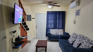 A living room with a TV, a ceiling fan, a sofa, a coffee table, and a door. - Residencia Mejía · Descanso y Comodidad a Minutos del Mar Caribe (Playa del Carmen)