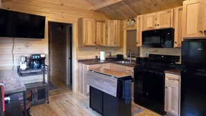 Une cuisine moderne avec des meubles en bois, un îlot central, un réfrigérateur noir, un four à micro-ondes et une machine à café.