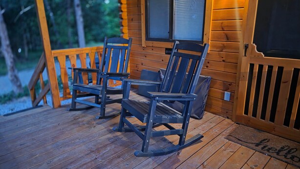 Une véranda en bois avec deux fauteuils à bascule et un paillasson sur lequel est écrit « Bonjour ».