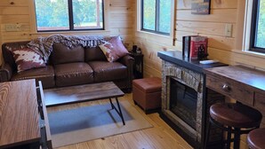 L’intérieur de la cabane est en bois, avec un canapé en cuir marron, un petit coin cuisine doté d’une cheminée en pierre et de grandes fenêtres.
