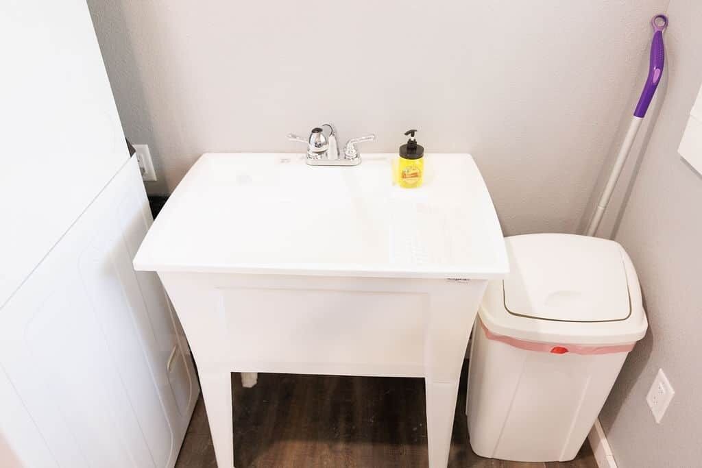 Un bagno piccolo e bianco con un lavandino, una bottiglia di sapone per le mani e un cestino.