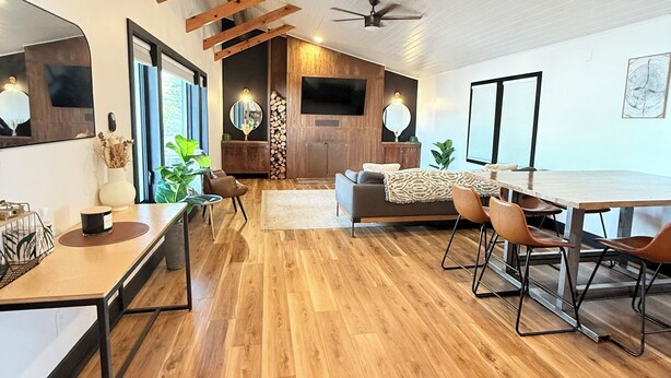 A modern living room with wooden flooring, a dining area, and a TV mounted on the wall.