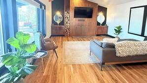 A modern living room with wooden floors, a sofa, a chair, a coffee table, and a TV mounted on the wall.