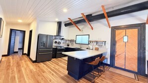 A modern kitchen with a central island, black appliances, and wooden flooring.
