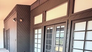 A room with a dark wooden floor, a patterned rug, and large windows with blinds.