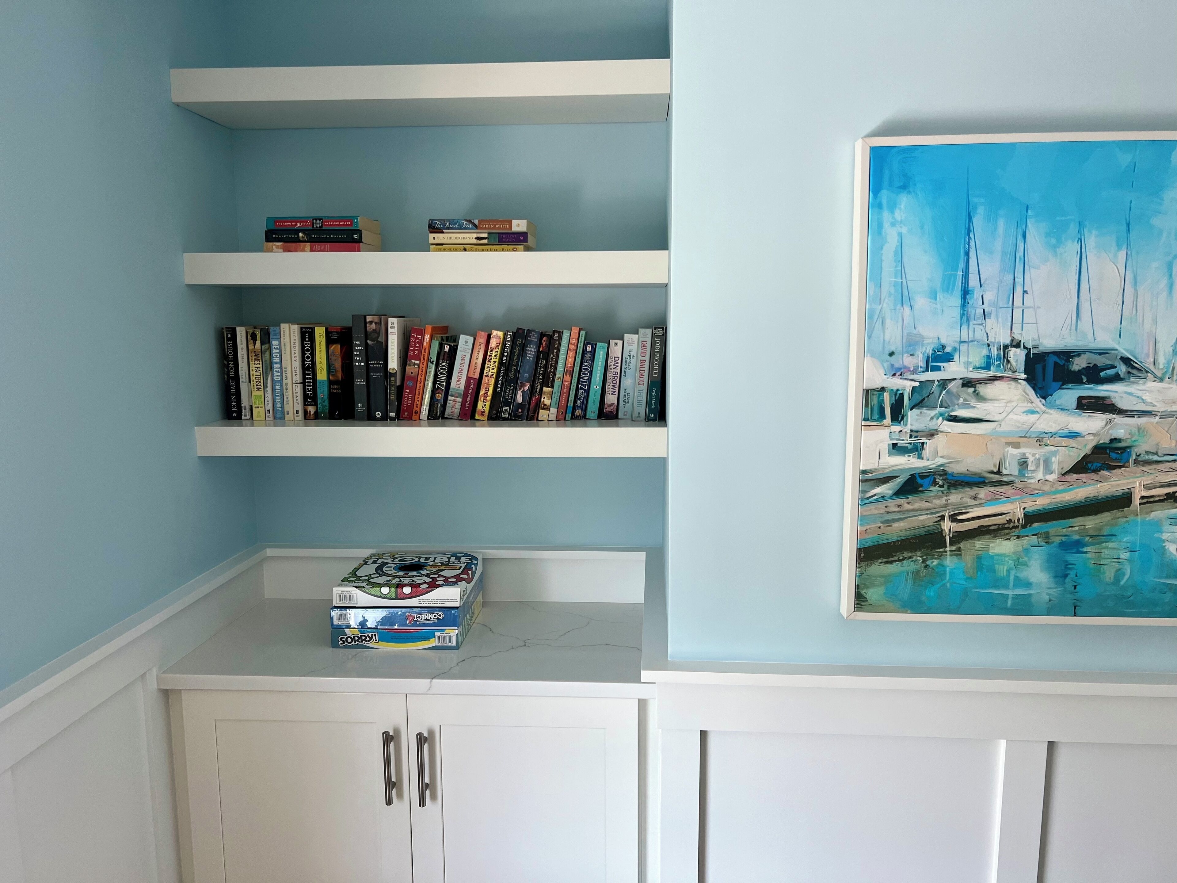 Ein Zimmer mit Bücherregal, einem Bootsgemälde und einem Schrank.