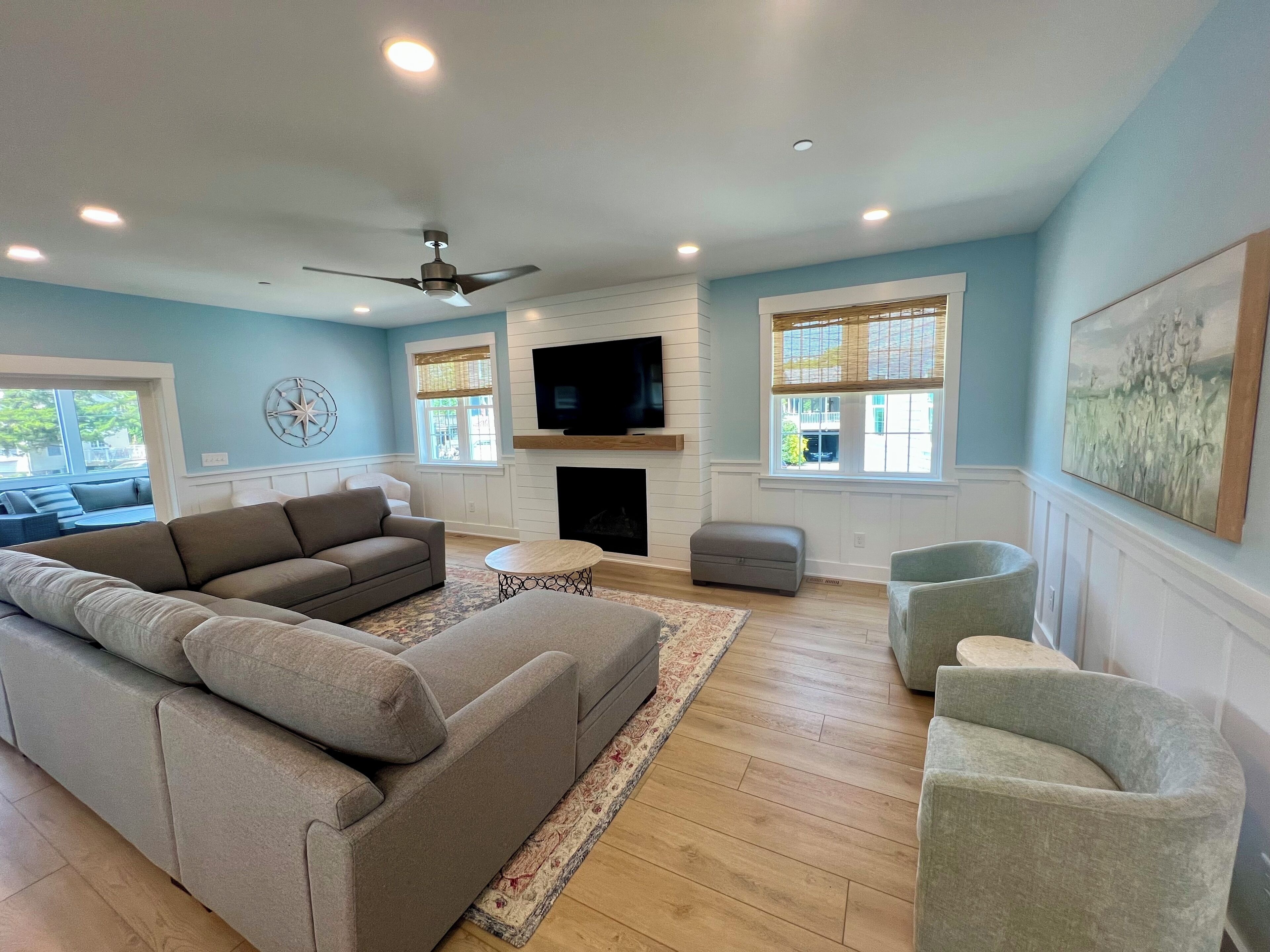 A spacious living room with a large sectional sofa, a fireplace, a flat-screen TV, and a ceiling fan.