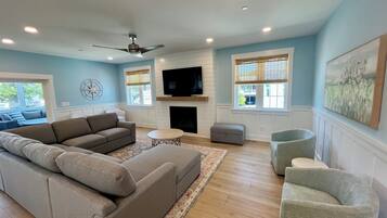 A spacious living room with a large sectional sofa, a fireplace, a flat-screen TV, and a ceiling fan.