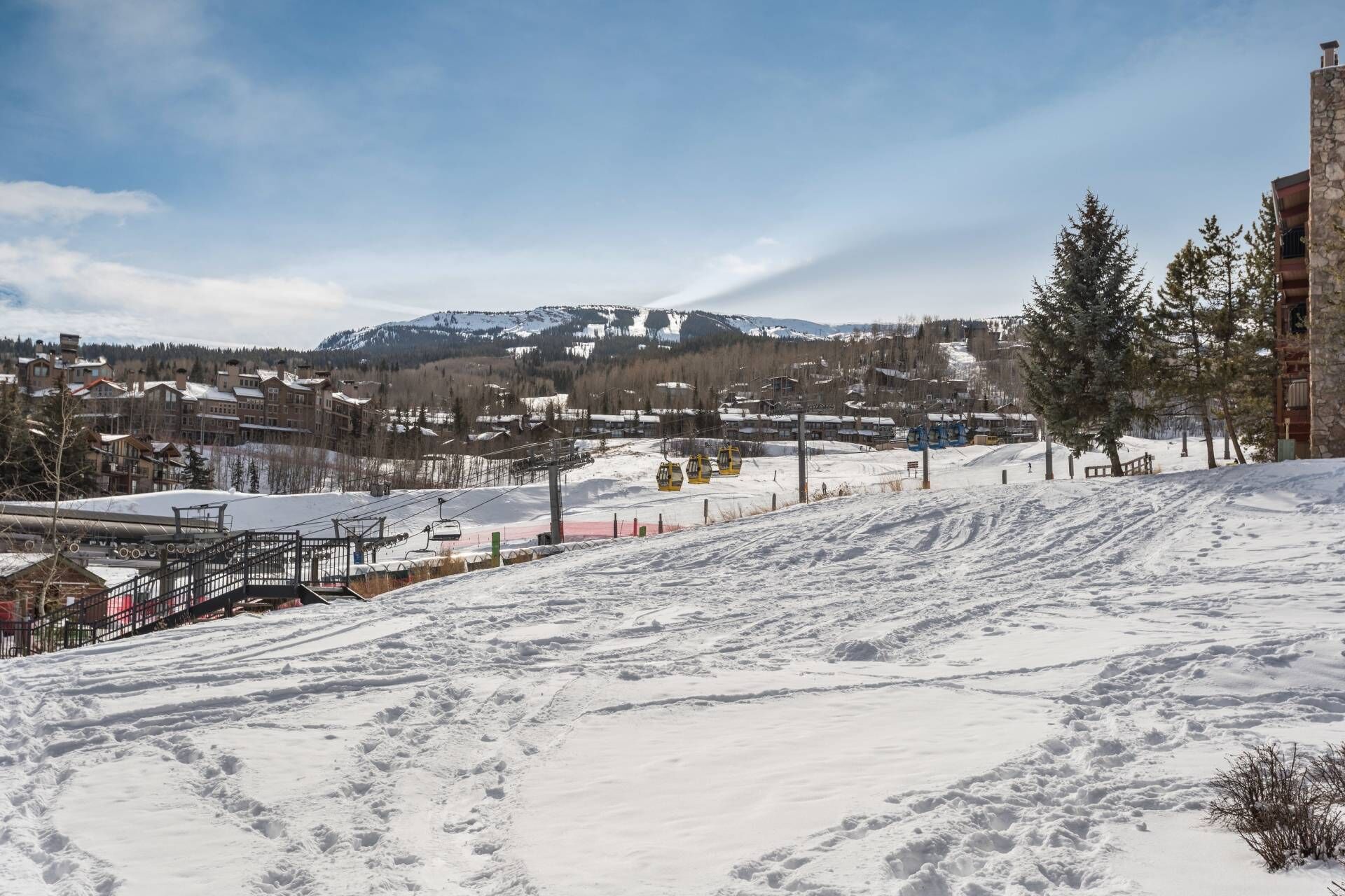 Ein verschneiter Skipisten mit Seilbahnen und Gebäuden im Hintergrund.