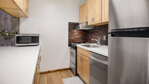 A modern kitchen with wooden cabinets, a stainless steel refrigerator, a microwave, a stove, and a sink. - Lichenhearth 29 (Snowmass Village)