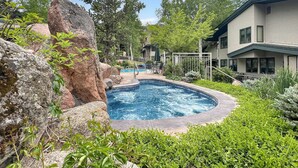 En swimmingpool omgiven av stenar och grönska, med ett hus i bakgrunden.