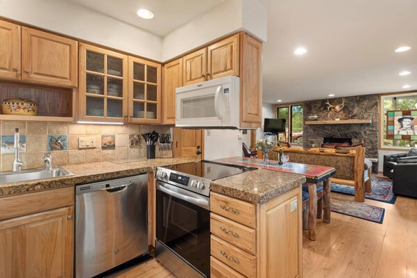 A modern kitchen with wooden cabinets, a built-in microwave, stainless steel appliances, and a stone fireplace.