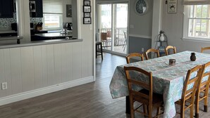 Una cocina amplia con armarios blancos, un comedor con una mesa dispuesta para seis personas y un ventilador de techo.