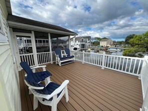 A wooden deck with white railings, two Adirondack chairs, and a covered area with a table and chairs.