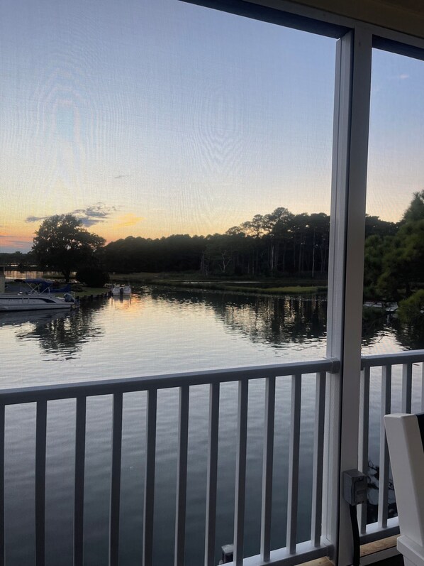 A view from a balcony overlooking a calm body of water with trees and a dock in the background.