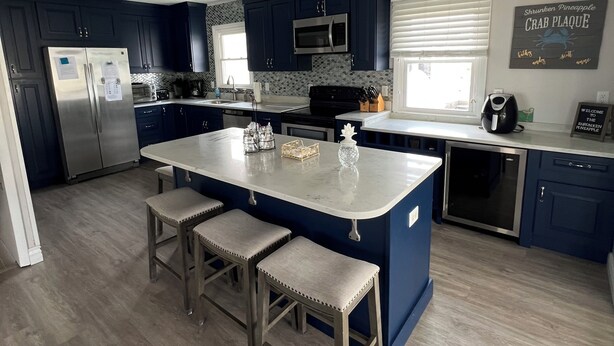Una cocina moderna con armarios azul oscuro, un refrigerador de acero inoxidable, un microondas y un horno empotrado. Cuenta con una isla grande con taburetes de bar, y un ventilador de techo.