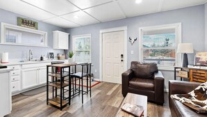 A modern kitchen with white cabinets, a dining area with a wooden table and chairs, a leather sofa, and a coffee table. - The Horseshoe Hideaway - Rodeo Themed & 1/2 mile walk to Whiskey Row! (Prescott)