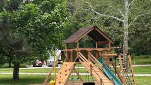 Une structure de jeux en bois comprenant un toboggan, un mur d’escalade et une balançoire.
